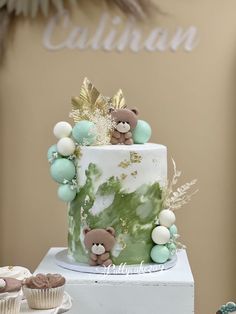 there is a green and white cake with teddy bears on the top, surrounded by cupcakes