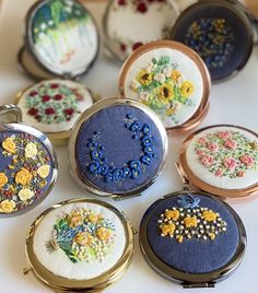 nine embroidered compact cases sitting on top of a white table with flowers and beads in them