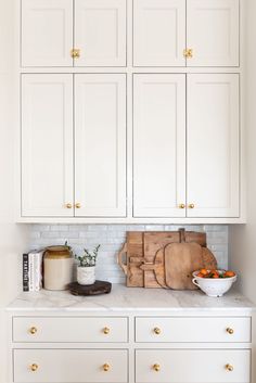 a kitchen with white cabinets and wooden cutting boards on the counter top next to a bowl of fruit