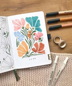 an open notebook with watercolor flowers on it next to crayons and markers