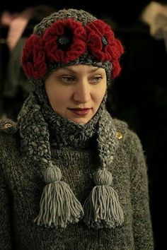 a woman wearing a knitted hat and scarf with flowers on the top, standing in front of other people