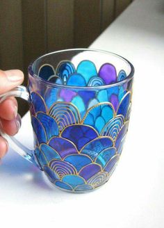 a hand holding a glass cup with blue and purple designs on it, sitting on a table