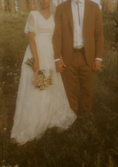 a man and woman standing next to each other in a field with trees behind them