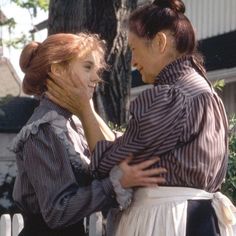 two women standing next to each other in front of a tree and fence with their heads together