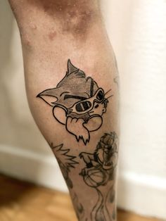 a tattoo on the leg of a man with a cat and flowers around his ankles