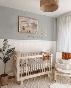 a baby's room with a crib, rocking chair and potted plant