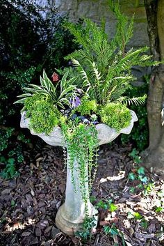 a planter with plants in it sitting on the ground next to a tree and shrubbery