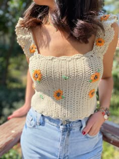 a woman wearing an off the shoulder top with sunflowers on it, standing next to a wooden bench