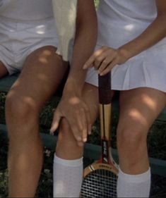 two women sitting on a bench holding tennis racquets