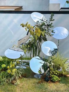 several mirrors sitting on top of a grass covered field next to trees and bushes in front of a building