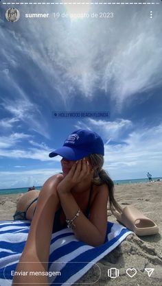 a woman laying on top of a blue and white towel under a sky filled with clouds