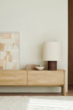 a wooden dresser with a lamp on top of it next to a painting and rug