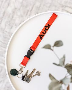 a red lanyard with keys on it sitting on top of a white plate next to a plant