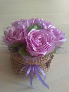 a crocheted basket with purple roses in it sitting on a table next to a ribbon