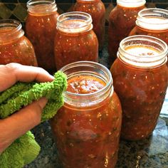 a hand is holding a green rag next to jars of pickled vegetables and sauce