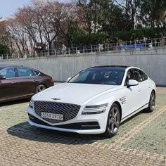 two white cars parked next to each other on a cobblestone street with trees in the background