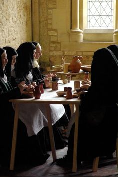 a group of people sitting around a table with cups and vases on top of it