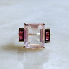 ITEM DESCRIPTION: >> The Ring is made from Solid 14K Yellow Gold. Gemstone used is absolutely natural and ethically sourced. >> Natural Rose Quartz & Rhodolite Garnet in prong setting is studded on it with utmost precision. >> This is a minimalist design which makes it a hassle free and everyday jewelry. >>Center Gem: Rose Quartz Center Gem size: 12x10 mm Center Gem weight: 5.70 ct >>Side gemstone: Rhodolite Garnet Side Gems size: 6x3 mm Gem weight: 1.15 carats Gold purity: 14K (58.33% approx.) Elegant Pink Topaz Ring In 14k Gold, Pink Three Stone Ruby Ring, Elegant Pink Ruby Three Stone Ring, Elegant Pink Three-stone Ruby Ring, Elegant Pink Three Stone Rings, Elegant Rose Gold Multi-stone Amethyst Ring, Morganite Rings With Gemstone Accents, Fine Jewelry, Formal Morganite Rings With Gemstone Accents, Formal Morganite Ring With Gemstone Accents