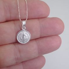 St. Benedict full-body image and a cross in the back Material that is extremely durable and hypoallergenic A powerful message of spiritual protection The front and back of this pendant are finely detailed, and the chain that it hangs from is no exception. The delicate details are embossed in a silver tone for better shine and shadowing for better contrast. This double-sided necklace is a must-have accessory. Pair this with any other necklace for a stylish and modern look. Dimensions & Specificat Symbolic Sterling Silver Charm Necklace With Coin Pendant, Spiritual Silver Jewelry With Coin Pendant, Sterling Silver Coin Medallion Necklace Nickel Free, Spiritual Sterling Silver Nickel-free Charm Necklace, Silver Miraculous Medal Jewelry As Gift, Silver Jewelry With Miraculous Medal For Gift, Spiritual Sterling Silver Nickel Free Charm Necklace, Silver Miraculous Medal Round Pendant, Silver Coin Medallion Necklace For Gift