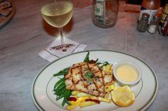 a white plate topped with meat and veggies next to a glass of wine