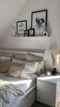 a white bed sitting in a bedroom next to a lamp and pictures on the wall