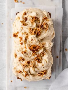 two slices of carrot cake with cream cheese frosting and walnuts on parchment paper