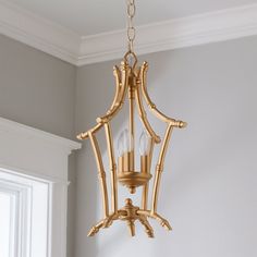 a golden chandelier hanging from the ceiling in a room with white walls and windows