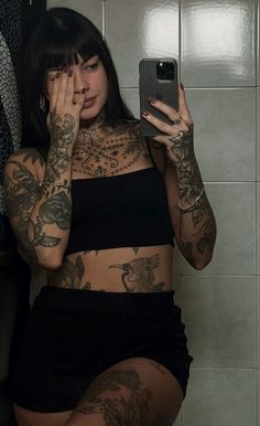 a woman with tattoos is taking a selfie in front of a mirror while holding her phone