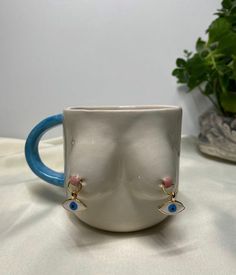 a white mug with blue handles sitting on a table next to a potted plant