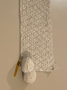 a white crocheted scarf hanging on a wall with a ball of yarn and a pair of scissors