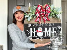 a woman holding up a welcome sign in front of a door with christmas decorations on it