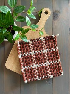 a wooden cutting board with a brown and white checkered cloth on it next to a potted plant