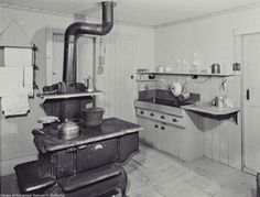 black and white photograph of an old fashioned kitchen with stove, sink, and oven