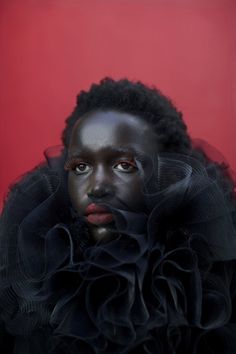 a woman with dark makeup and black hair wearing a ruffled dress against a red background