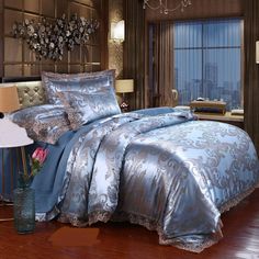 a bed with blue and silver comforters in a room next to a window,