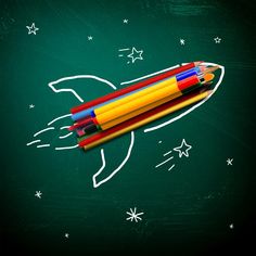 three colored pencils in the shape of a rocket on a green chalkboard with stars