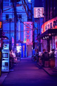 an alley way at night with neon signs on the buildings