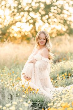 a pregnant woman standing in a field of flowers at sunset with the sun shining on her belly