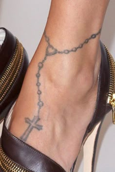 a close up of a person's foot with a cross tattoo on the ankle