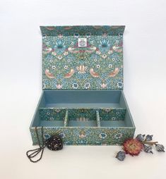 an open jewelry box sitting on top of a white table next to a dried flower