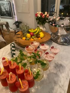 a table topped with cups filled with drinks and fruit next to bowls of food on top of a counter