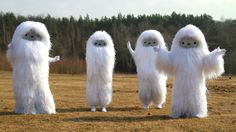 three white fluffy creatures standing next to each other on a field with trees in the background