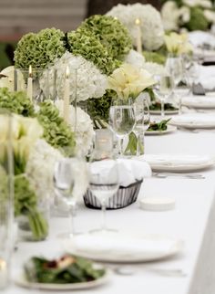 a long table is set with white flowers and candles for an elegant dinner or party