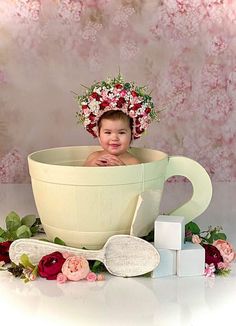 a baby is sitting in a large bowl with flowers on her head, surrounded by other items