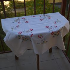 a white table cloth with red flowers on it sitting on a balcony overlooking the trees