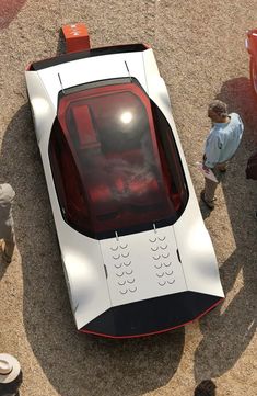 an overhead view of a futuristic car on the ground with people standing around and looking at it