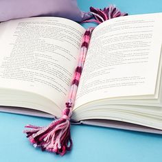 an open book sitting on top of a table next to a purple pillow and some tassels