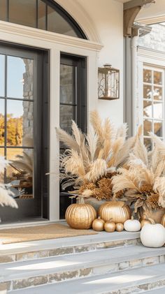 the front porch is decorated with gold and white pumpkins, pamodia plants, and ornamental urns