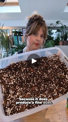 a woman holding up a container filled with dirt