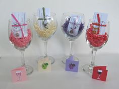 four wine glasses with different types of candy in them and cards attached to the rims